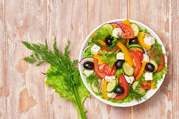 Greek salad with cucumeber, olives, feta cheese, cherry tomatoes, bell pepper, onion and lettuce. Diet, vitamin food. Healthy vegetarian meal concept. Tasty salad in bowl on wood, top view.