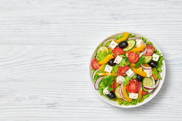 Greek salad with cucumeber, olives, feta cheese, cherry tomatoes, bell pepper, onion and lettuce. Diet, vitamin food. Healthy vegetarian meal concept. Tasty salad in bowl on wood, top view. Copy space