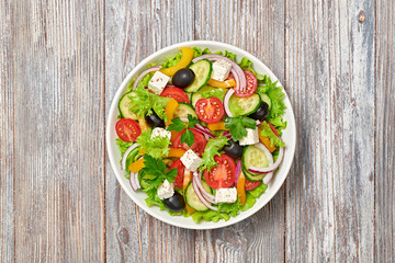 Greek salad with cucumeber, olives, feta cheese, cherry tomatoes, bell pepper, onion and lettuce. Diet, vitamin food. Healthy vegetarian meal concept. Tasty salad in bowl on wood, top view. Copy space
