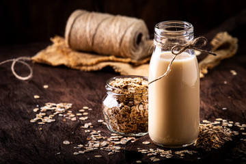Oat flakes milk, non dairy alternative plant based drink in glass, wooden rustic kitchen table, copy space
