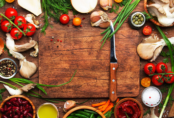 Food cooking background, ingredients for preparation vegan dishes, vegetables, roots, spices, mushrooms and herbs. Cutting board, chef knife. Healthy food concept. Rustic wooden table, top view