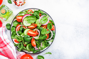 Spring vegan salad with spinach, cherry tomatoes, corn salad, baby spinach, cucumber and red onion. Healthy food concept. Gray stone table. Top view. Copy space