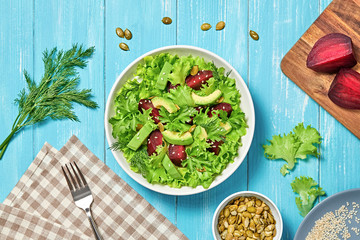 Vegan beetroot salad, avocado, lettuce, sunflower, sesame seed. Home made vegetarian beet salad. Clean eating concept on wood background. Tasty fresh beetroot veg mix leaves dish, flat lay