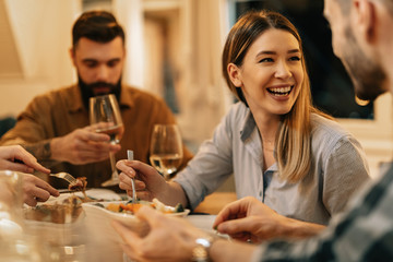 Cheerful woman talking to her friends while having dinner at dining table.