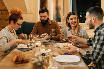 Group of happy friends talking and eating sinner at dining table.