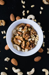 superfood concept, almond, cedar, walnuts, cashew nuts in a plate on a black background