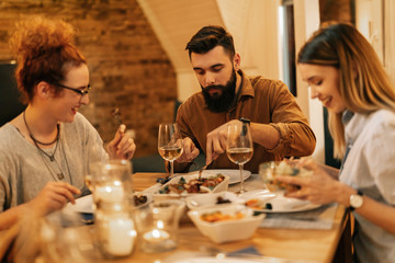 Small group of friends eating dinner at dining table at home.