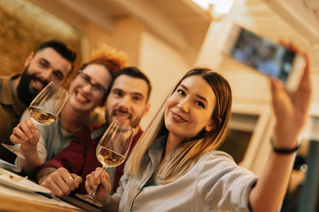 Group of happy friends taking selfie with smart phone at dining table.