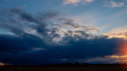 Dark rain clouds in the evening in the field. Panoramic landscape.