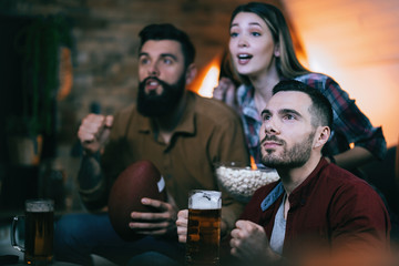 Small group of sport fans watching rugby match on TV at home.