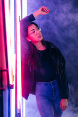 Fashion portrait of young elegant woman in sunglasses in a black cotton jacket on a neon background in smoke