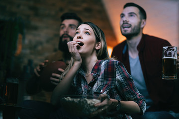 Excited woman and her friends watching sports match on TV at home.