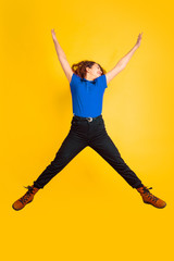 Fototapeta na wymiar Jumping, crazy happy. Caucasian teen's girl portrait on yellow studio background. Beautiful female curly model. Concept of human emotions, facial expression, sales, ad, education. Copyspace.