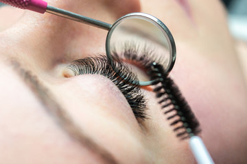 Woman getting eyelashes extension treatment / brushing eyelash extensions.