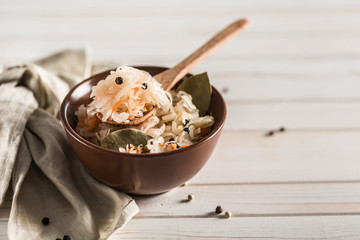 Fermented cabbage in a brown plate with a wooden spoon and a linen napkin on a light background.