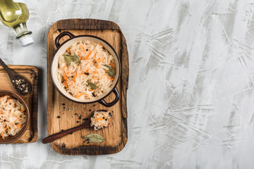 Fermented cabbage in a plate on a wooden tray with a spoon and a bottle of oil on a light background.