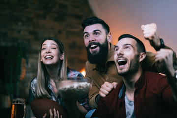 Group of cheerful friends watching sports championship on TV at home.