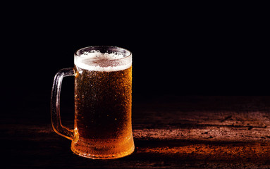 Beer. Cold Craft light Beer in a glass with water drops on the wooden table over the black background.