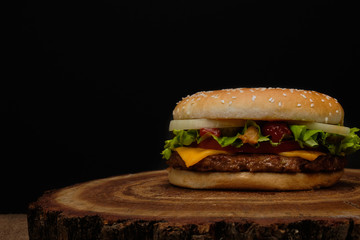 Big burger with beef buffet, cheese and herbs on a wooden tray in the form of a tree on a black background