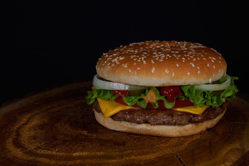 Big burger with beef buffet, cheese and herbs on a wooden tray in the form of a tree on a black background