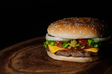 Big burger with beef buffet, cheese and herbs on a wooden tray in the form of a tree on a black background
