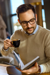 Elegant man reading a book and drinking coffee on the table in a restaurant.