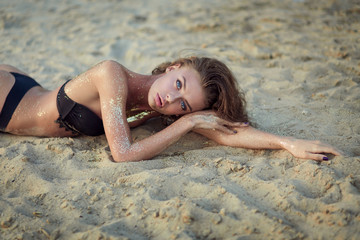 very beautiful woman with incredible blue eyes in black bikini the golden sand. Sensual portrait of amazing girl wet hair. Tan beach vacation spa. Sexy model portrait close-up. Glamor sparkles on body