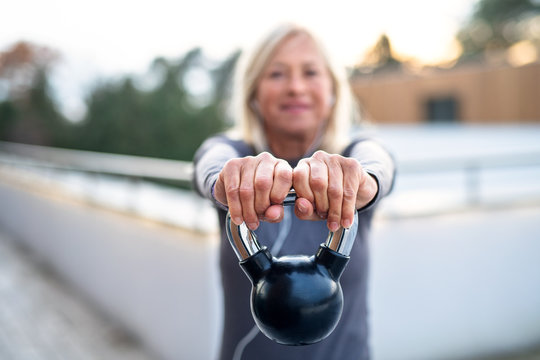 A Senior Woman With Kettlebell Outdoors Doing Exercise.