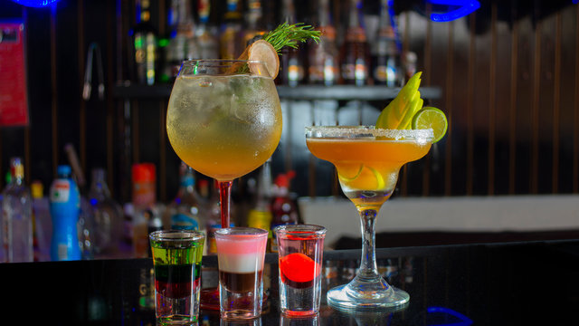 Glass Cup With Passion Fruit Margarita Accompanied By Three Small Glass Glasses With Tequila Reflecting On The Table Of A Bar