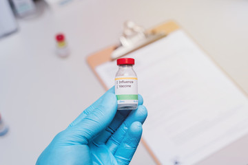 influenza vaccination concept doctor with blue gloves holding vaccine vial and clipboard with checklist in background