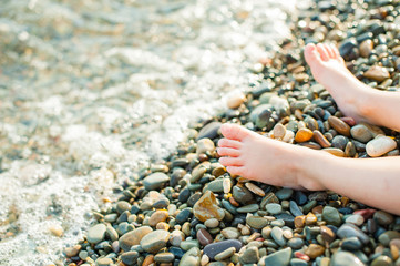 Child's feet on a beach in small color pebble in a summer sunny day. Holiday on a seashore.