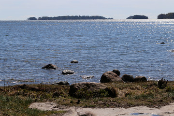 Beautiful calm Baltic Sea photographed in Espoo, Finland during a sunny summer day. The beach has a lot of medium sized rocks and some plants. You can also see some islands with forest in the horizon.