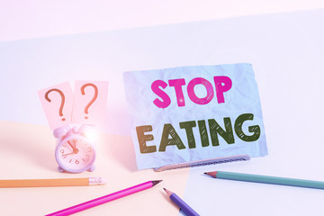 Word writing text Stop Eating. Business photo showcasing cease the activity of putting or taking food into the mouth Mini size alarm clock beside stationary placed tilted on pastel backdrop