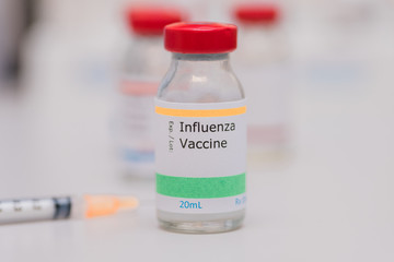 influenza vaccination concept with syringe and other vaccine vials in background