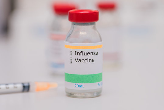 influenza vaccination concept with syringe and other vaccine vials in background