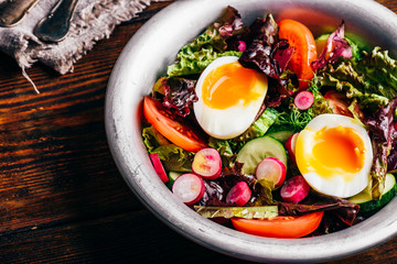 Fresh spring salad with tomato, radish, cucumber, red leaf lettuce and boiled eggs in metal bowl