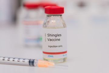 Shingles vaccine concept with syringe in foreground, vaccination vial on counter with additional...