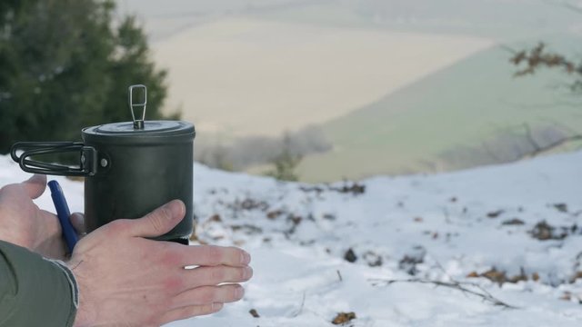 Adult Male Using Lighter To Light Portable Gas Stove Out On Snow Covered Hill With Countryside In The Distance. Locked Off 
