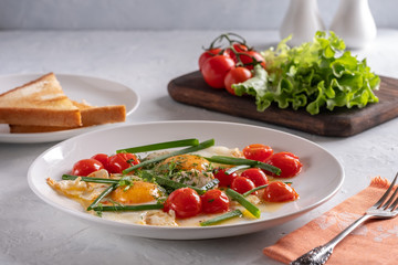 Fried eggs with cherry tomatoes and green onions on a white plate