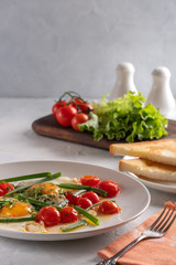 Fried eggs with cherry tomatoes and green onions on a white plate