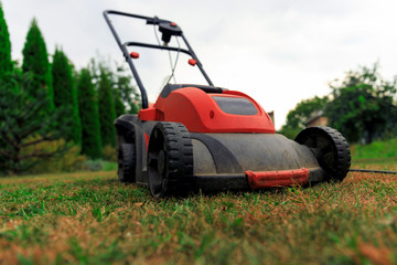 Obraz premium Lawn mower cutting green grass in backyard.Gardening background.
