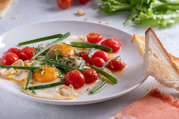 Fried eggs with cherry tomatoes and green onions on a white plate