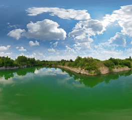 Abandoned quarry in the azure water, open pit mining in Ukraine. White soft clouds over the azure water of the flooded granite quarry. Around the cliffs and green trees and plants