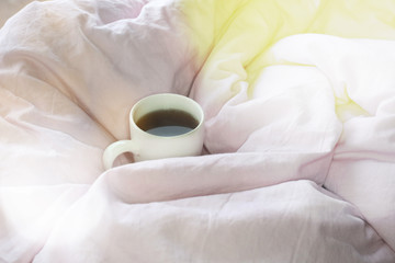 Fototapeta na wymiar Morning coffee mug in pink bed sheet background. Cotton textile waved.
