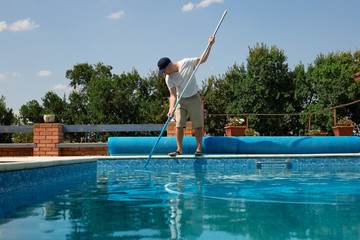 Cleaner of the swimming pool. Man cleaning outdoor swimming pool with vacuum tube cleaner in summer. Seasonal preparations.Cleaning systems for swimming pools.