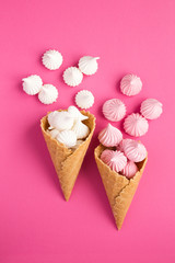 Two ice cream cones with white and pink meringue on the pink background. Location vertical. Top view.