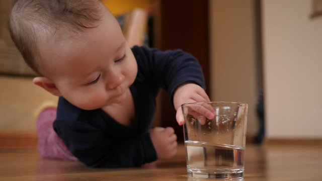 Toddler child awkwardly takes a glass of water and spills water on the floor at home