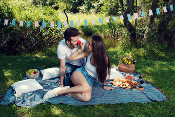 Playful young couple having picnic in city park He wears red nose Selective focus