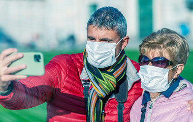 Fototapeta na wymiar Coronavirus alarm in Italy, Europe. Man with his mother wearing respirator mask visiting city park. New type Covid-19 virus has been spreading in many cities in Italy