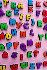 The multi-colored letters of the English alphabet are scattered on a pink background. Learning the alphabet. The concept of education in kindergarten and school. Alphabet for stores, sales, websites